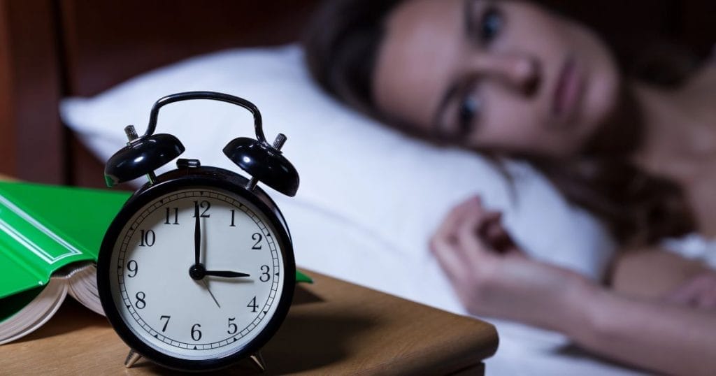 donna con insonnia a letto con sveglia che segna le tre di notte